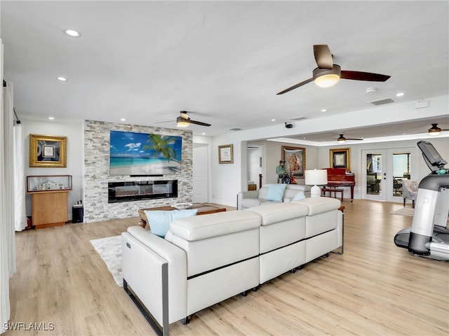 living area featuring a large fireplace, visible vents, light wood-type flooring, and ceiling fan