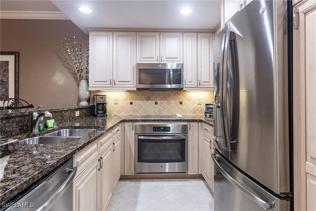 kitchen with backsplash, crown molding, dark stone counters, stainless steel appliances, and a sink