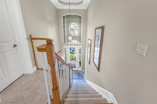 stairway featuring crown molding, baseboards, a towering ceiling, tile patterned floors, and a notable chandelier