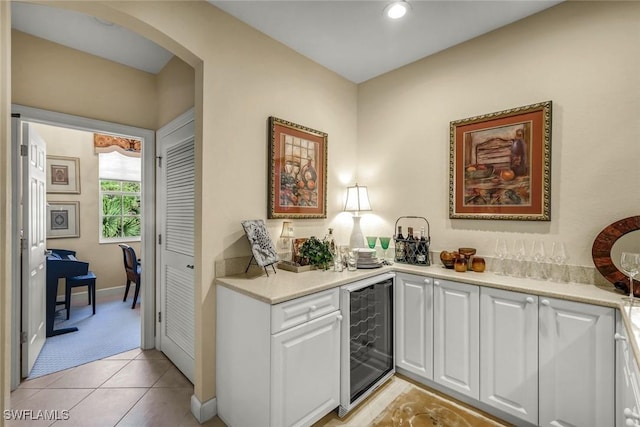 kitchen with white cabinetry, wine cooler, arched walkways, light tile patterned flooring, and light countertops