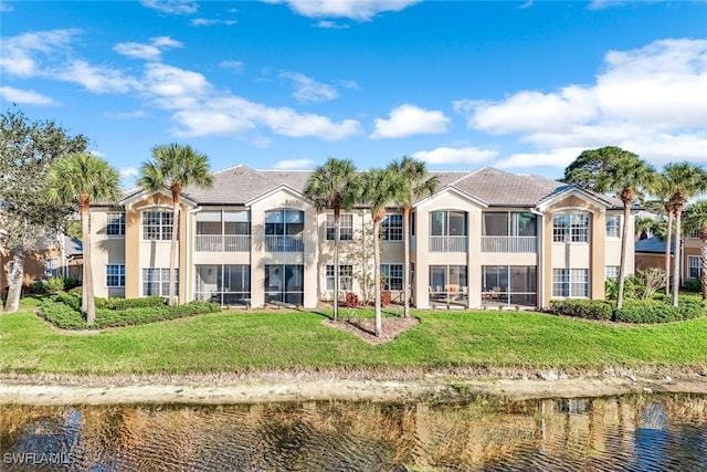 back of property with a yard, a water view, and stucco siding