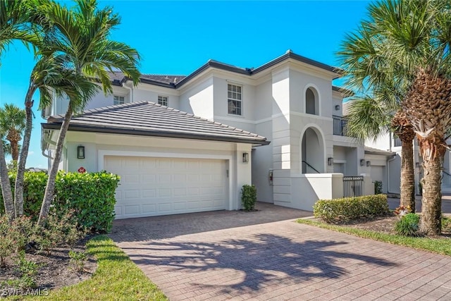 mediterranean / spanish-style house with a tiled roof, fence, an attached garage, stucco siding, and decorative driveway