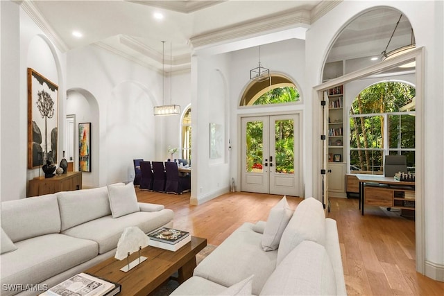 living room with light wood finished floors, french doors, a towering ceiling, and ornamental molding