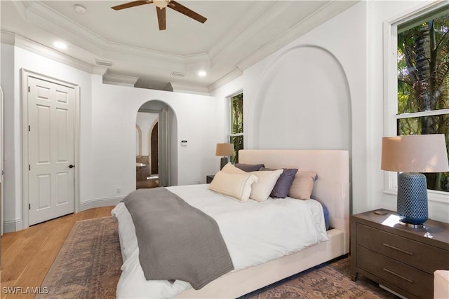 bedroom featuring wood finished floors, visible vents, arched walkways, crown molding, and connected bathroom