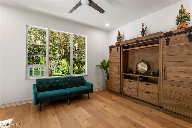 living area with light wood-style flooring, a ceiling fan, recessed lighting, a barn door, and baseboards