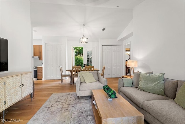 living area with light wood-style flooring, visible vents, and high vaulted ceiling