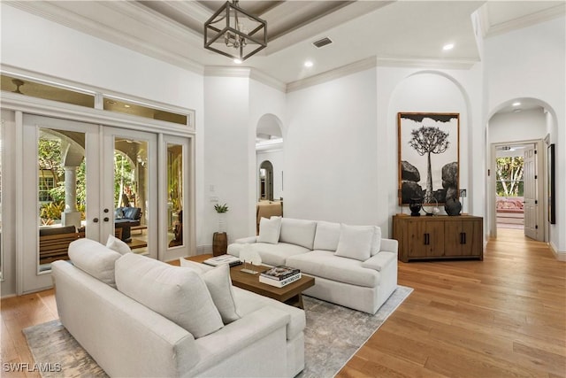 living room with visible vents, a high ceiling, arched walkways, crown molding, and light wood-type flooring