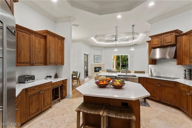 kitchen with ornamental molding, under cabinet range hood, built in fridge, black electric cooktop, and a raised ceiling