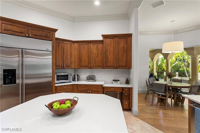 kitchen with hanging light fixtures, built in refrigerator, light countertops, and ornamental molding