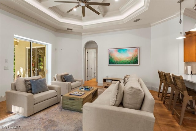 living area with light wood-style floors, crown molding, visible vents, and arched walkways