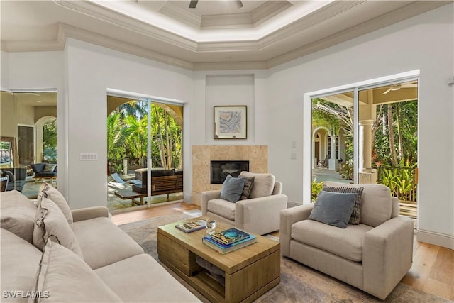 living area with a high end fireplace, crown molding, a towering ceiling, wood finished floors, and a ceiling fan