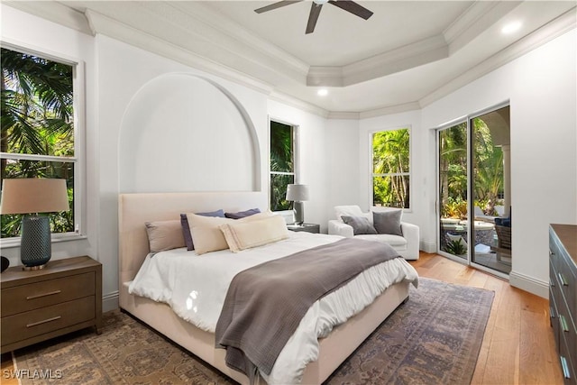 bedroom with crown molding, ceiling fan, a tray ceiling, light wood-style floors, and access to outside