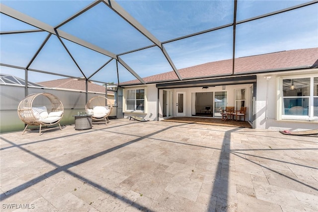 back of house featuring stucco siding, a shingled roof, glass enclosure, and a patio