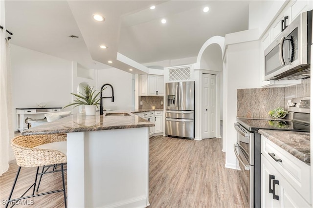 kitchen with dark stone counters, a kitchen bar, light wood-style flooring, stainless steel appliances, and a sink