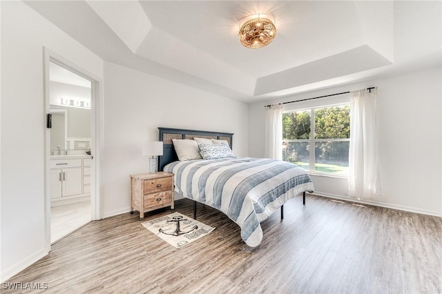 bedroom featuring connected bathroom, baseboards, a tray ceiling, wood finished floors, and a sink