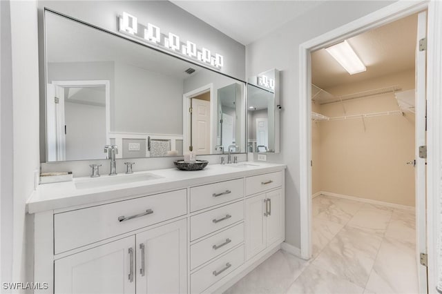 full bath featuring double vanity, a spacious closet, marble finish floor, and a sink