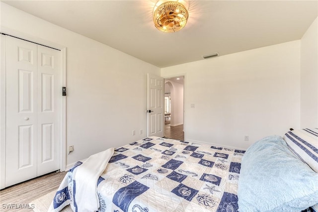 bedroom featuring wood finished floors, visible vents, arched walkways, and a closet