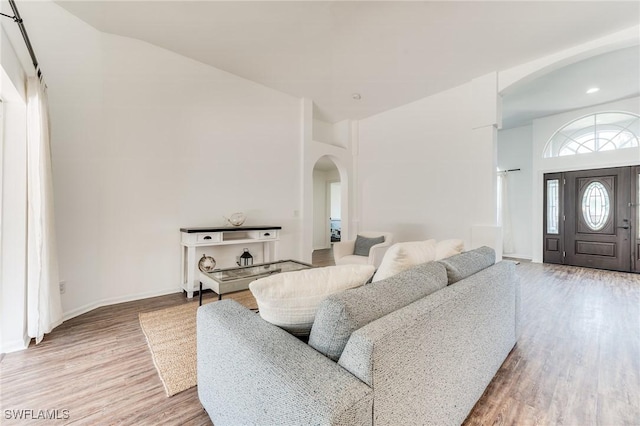 living room with high vaulted ceiling, wood finished floors, arched walkways, and baseboards