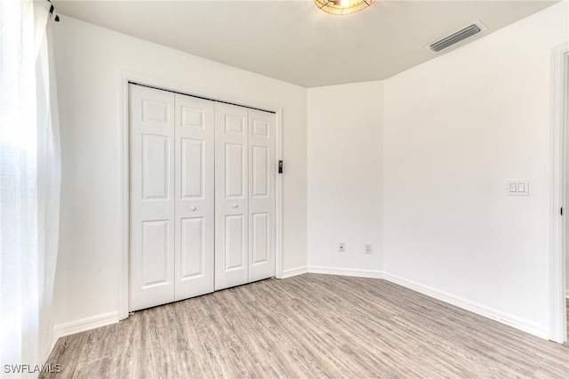 unfurnished bedroom with a closet, visible vents, baseboards, and light wood-style floors