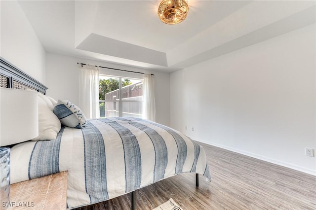 bedroom featuring a raised ceiling, baseboards, and wood finished floors