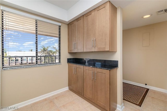 kitchen featuring light tile patterned floors, visible vents, dark stone countertops, and baseboards