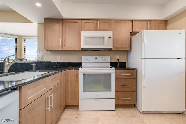 kitchen with a sink, dark stone counters, white appliances, and light tile patterned floors