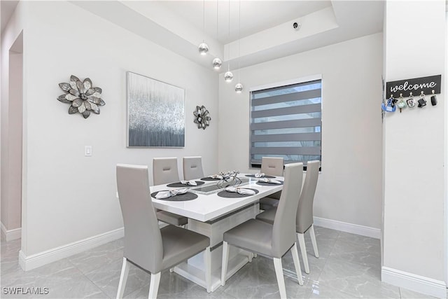 dining space featuring marble finish floor, a tray ceiling, and baseboards