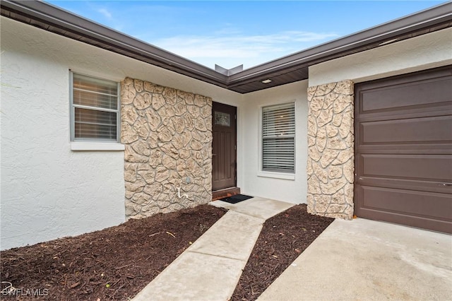 view of exterior entry featuring stucco siding, stone siding, and an attached garage