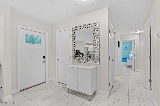 foyer entrance with baseboards, marble finish floor, and a textured ceiling