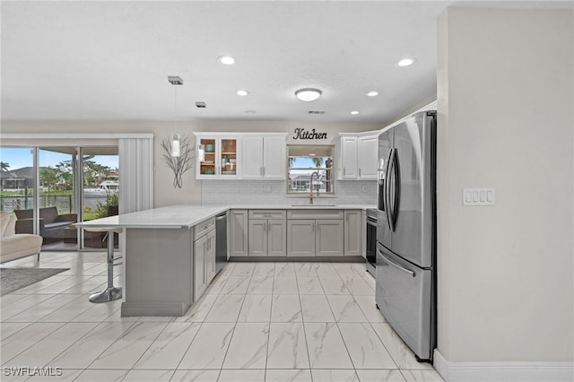 kitchen featuring light countertops, a peninsula, marble finish floor, stainless steel appliances, and a sink