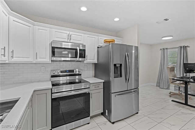 kitchen featuring white cabinetry, tasteful backsplash, marble finish floor, and stainless steel appliances