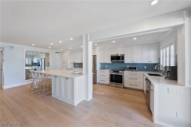 kitchen with crown molding, light wood finished floors, appliances with stainless steel finishes, and a sink