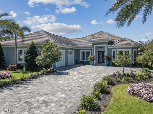 view of front of property with a tile roof, decorative driveway, a garage, and stucco siding