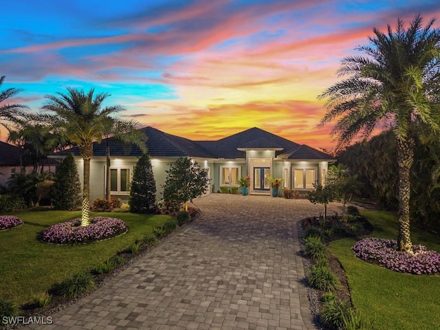 prairie-style home with a tiled roof, a yard, decorative driveway, and stucco siding