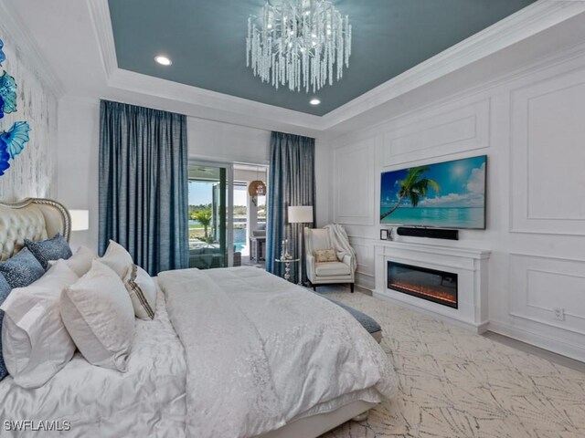 bedroom with an inviting chandelier, a tray ceiling, a glass covered fireplace, crown molding, and a decorative wall