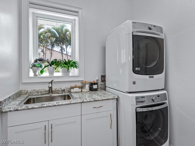 clothes washing area with a sink, cabinet space, and stacked washing maching and dryer