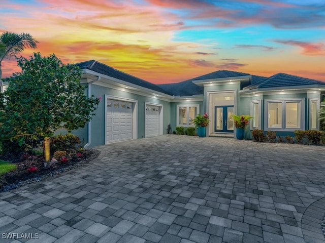 prairie-style home with stucco siding, french doors, a garage, a tile roof, and decorative driveway