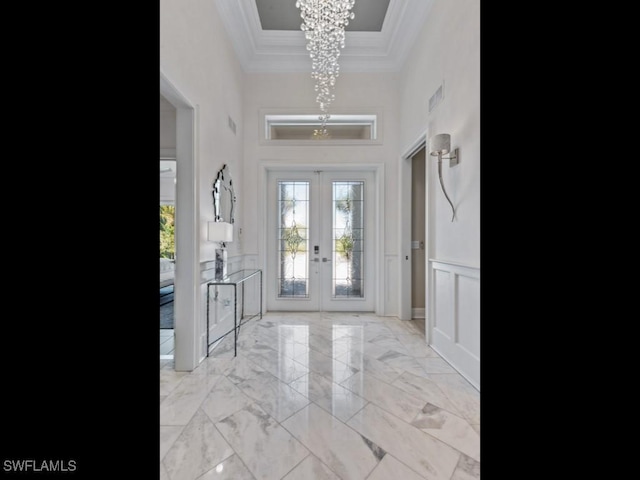 entrance foyer with ornamental molding, french doors, wainscoting, a decorative wall, and a chandelier