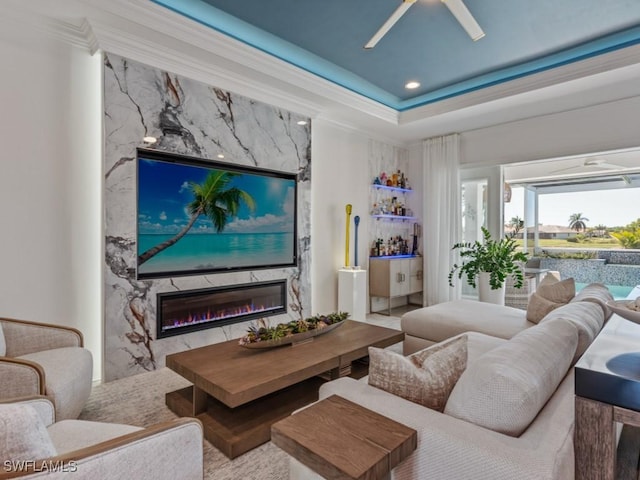 living room featuring a high end fireplace, ceiling fan, a tray ceiling, ornamental molding, and recessed lighting