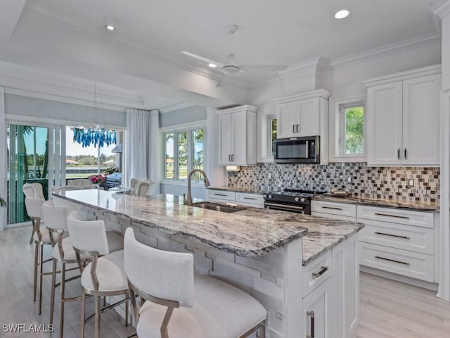 kitchen featuring stainless steel microwave, decorative backsplash, black range oven, white cabinets, and a sink