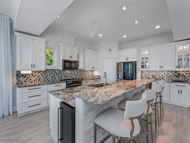 kitchen featuring glass insert cabinets, gas range oven, black fridge, white cabinetry, and a sink