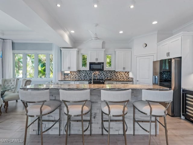 kitchen with white cabinets, fridge with ice dispenser, black microwave, and a kitchen island with sink