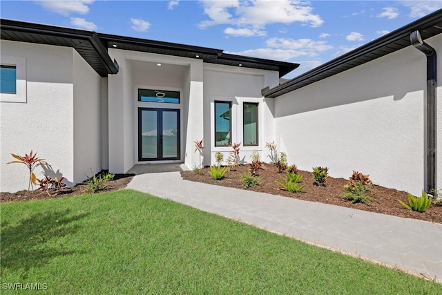 view of exterior entry featuring stucco siding and a yard