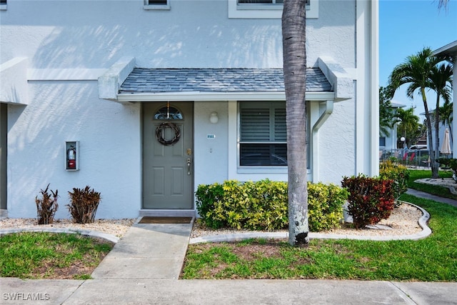 doorway to property with stucco siding and roof with shingles