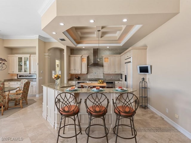 kitchen featuring a breakfast bar area, visible vents, ornamental molding, a large island, and wall chimney exhaust hood