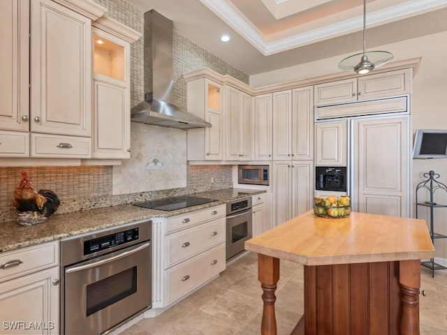 kitchen with cream cabinetry, tasteful backsplash, appliances with stainless steel finishes, butcher block counters, and wall chimney range hood