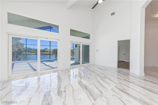 empty room featuring a ceiling fan, beam ceiling, a high ceiling, a water view, and marble finish floor