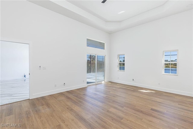 unfurnished room featuring a high ceiling, light wood finished floors, baseboards, and a wealth of natural light