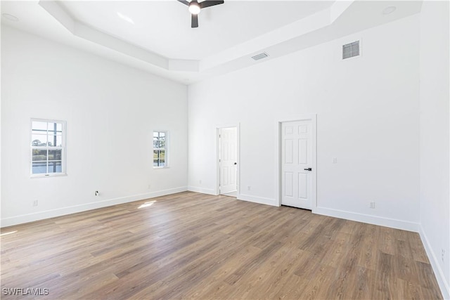 empty room featuring a tray ceiling, wood finished floors, visible vents, and baseboards