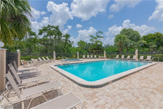 pool with a patio, a community hot tub, and fence